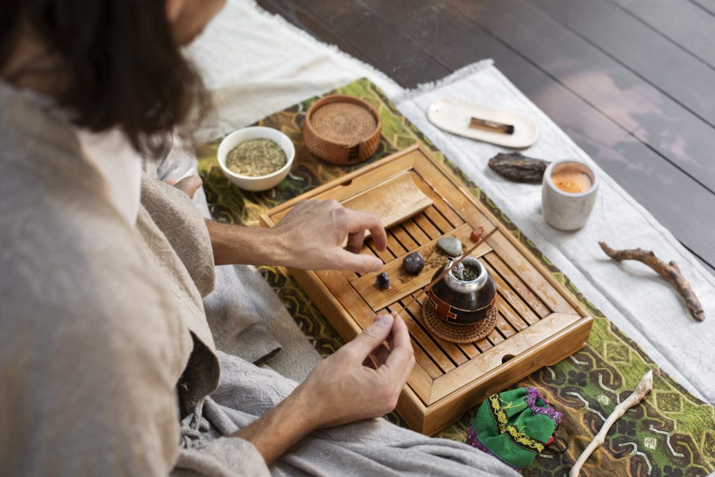 Person preparing a traditional tea ceremony on a wooden tray with herbal ingredients and accessories around