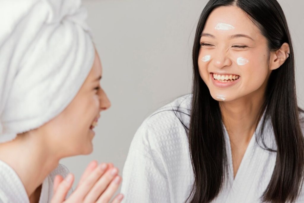 Two women in white robes smiling with face cream, enjoying a relaxing spa day